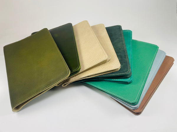 A fan arrangement of leather folio-style covers in multiple colors, including olive green, dark green, beige, teal, mint green, light blue, and brown, photographed on a clean white background.